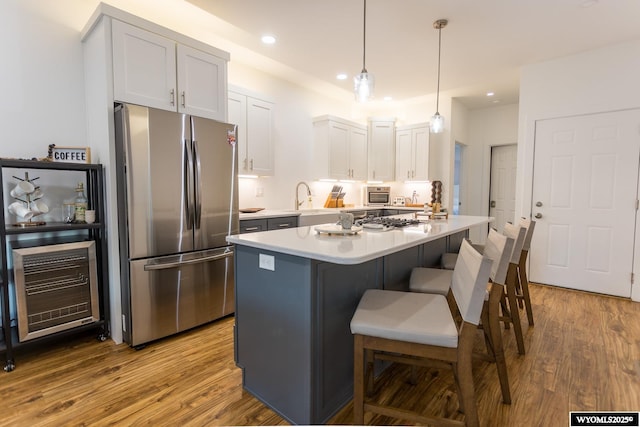 kitchen with stainless steel refrigerator, decorative light fixtures, hardwood / wood-style floors, and white cabinets