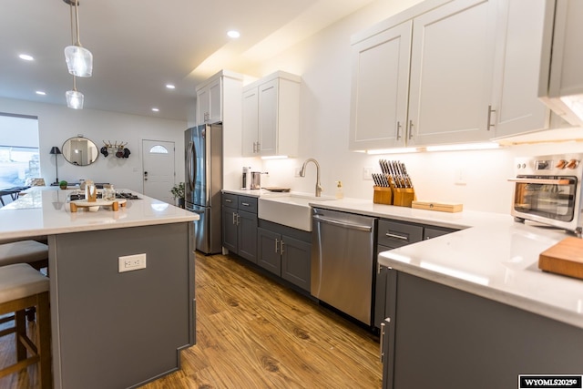 kitchen with sink, appliances with stainless steel finishes, hanging light fixtures, a kitchen breakfast bar, and white cabinets