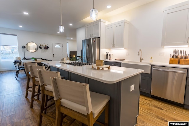 kitchen featuring a kitchen bar, sink, appliances with stainless steel finishes, a kitchen island, and pendant lighting