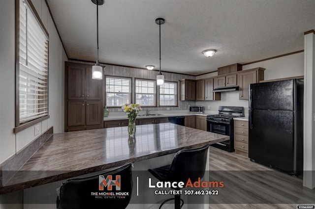 kitchen featuring a breakfast bar, black appliances, decorative light fixtures, kitchen peninsula, and light wood-type flooring