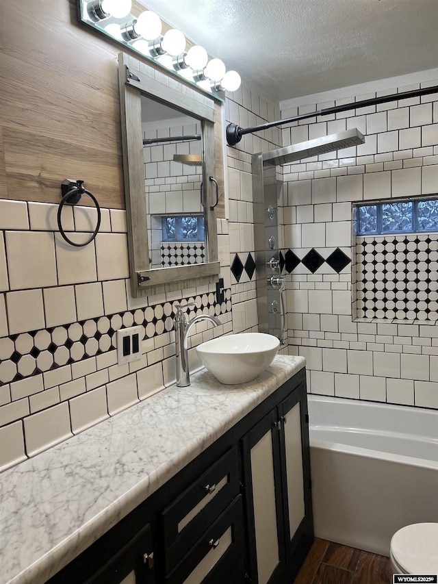 full bathroom featuring hardwood / wood-style floors, vanity, tasteful backsplash, tiled shower / bath, and toilet