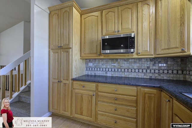 kitchen featuring light brown cabinets, stainless steel microwave, decorative backsplash, and dark stone counters