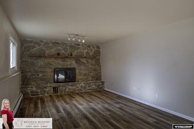 unfurnished living room featuring a stone fireplace, baseboard heating, wood finished floors, and baseboards