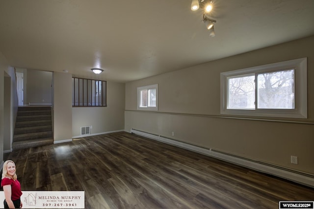 empty room featuring a baseboard heating unit, visible vents, baseboards, stairway, and dark wood finished floors