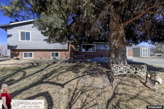 split level home featuring brick siding, a storage unit, and an outbuilding