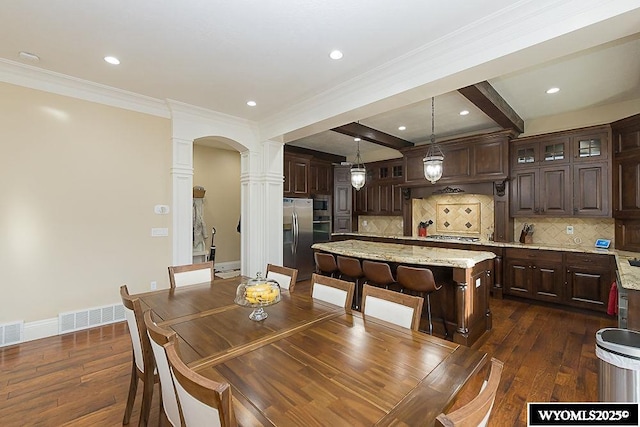 dining space with ornamental molding, dark hardwood / wood-style floors, beam ceiling, and ornate columns