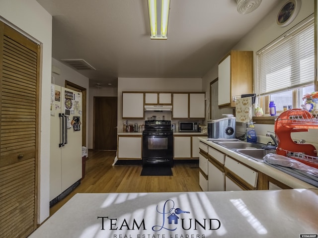 kitchen with black electric range oven, sink, light hardwood / wood-style flooring, white fridge, and white cabinets