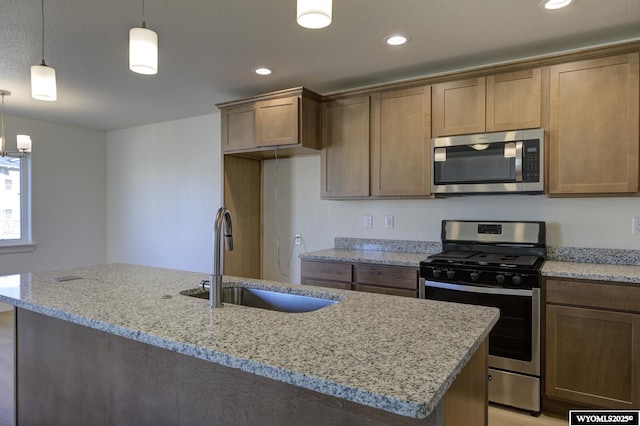 kitchen featuring hanging light fixtures, light stone countertops, appliances with stainless steel finishes, and sink