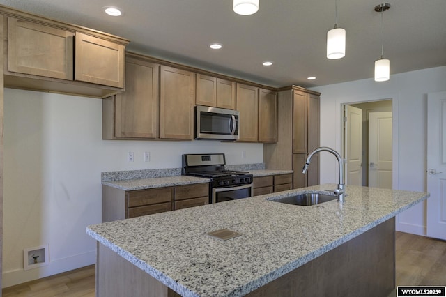 kitchen featuring appliances with stainless steel finishes, decorative light fixtures, sink, light stone counters, and a center island with sink