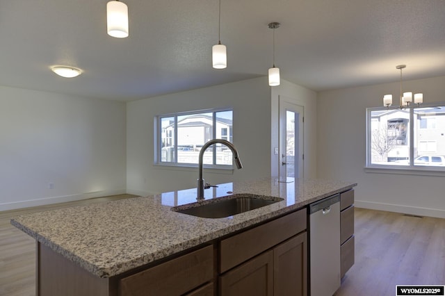 kitchen featuring sink, light hardwood / wood-style flooring, a kitchen island with sink, light stone counters, and stainless steel dishwasher