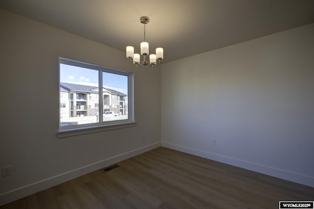 spare room with dark hardwood / wood-style floors and a notable chandelier