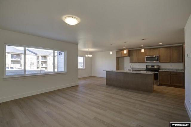 kitchen with hanging light fixtures, wood-type flooring, appliances with stainless steel finishes, and a center island with sink