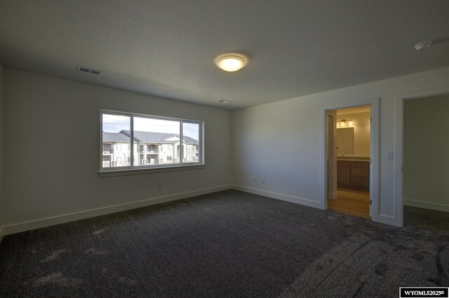 unfurnished bedroom with ensuite bath, a textured ceiling, and dark colored carpet