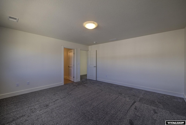 spare room featuring a textured ceiling and dark colored carpet