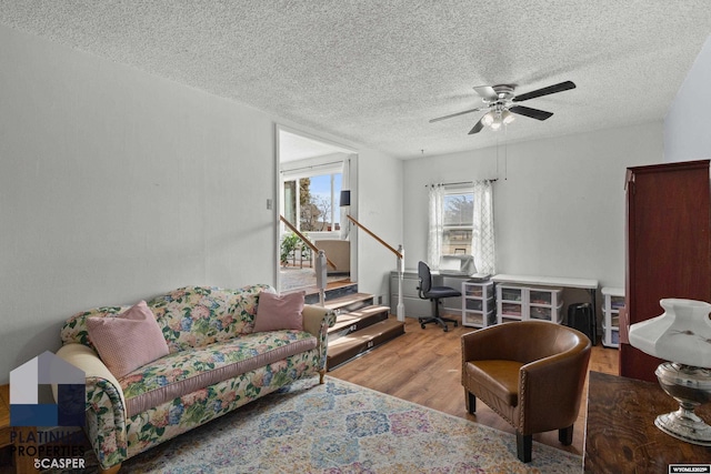 living room with ceiling fan, a textured ceiling, and light hardwood / wood-style floors