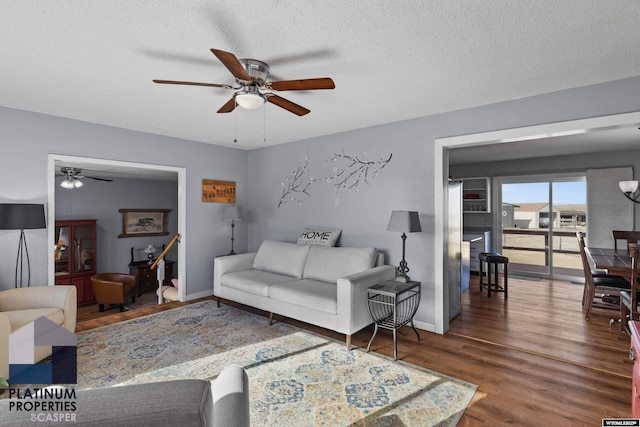 living room featuring dark wood-type flooring, ceiling fan, and a textured ceiling