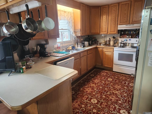 kitchen with under cabinet range hood, a peninsula, white appliances, light countertops, and brown cabinetry