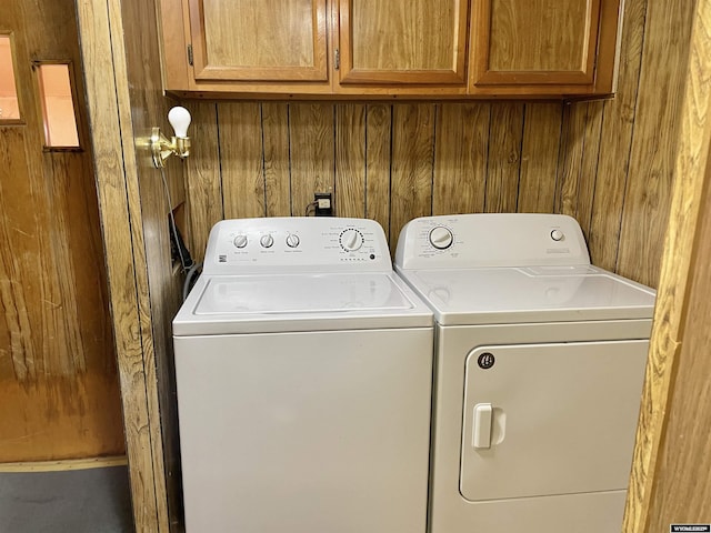 clothes washing area featuring cabinets, separate washer and dryer, and wood walls