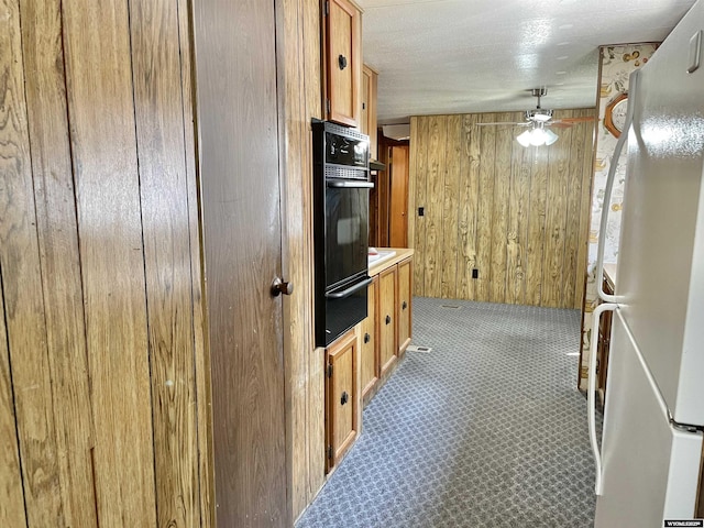 kitchen featuring black oven, wood walls, white fridge, carpet, and ceiling fan