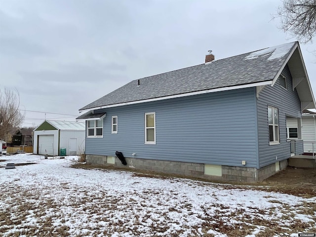 snow covered rear of property featuring an outbuilding and a garage