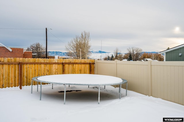 snowy yard featuring a trampoline and a mountain view