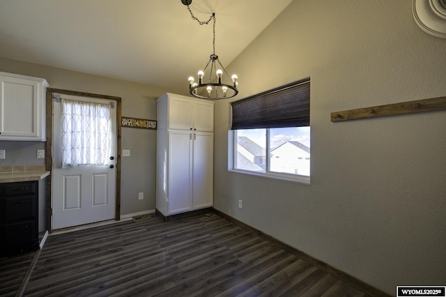 unfurnished dining area featuring lofted ceiling, dark hardwood / wood-style floors, and a notable chandelier