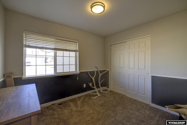 unfurnished bedroom with wooden walls, a closet, and carpet