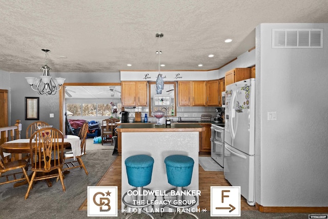 kitchen featuring an inviting chandelier, decorative light fixtures, a center island, a textured ceiling, and white appliances