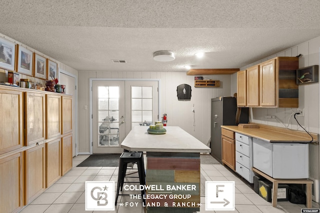 kitchen with stainless steel fridge, a textured ceiling, light tile patterned flooring, french doors, and light brown cabinets