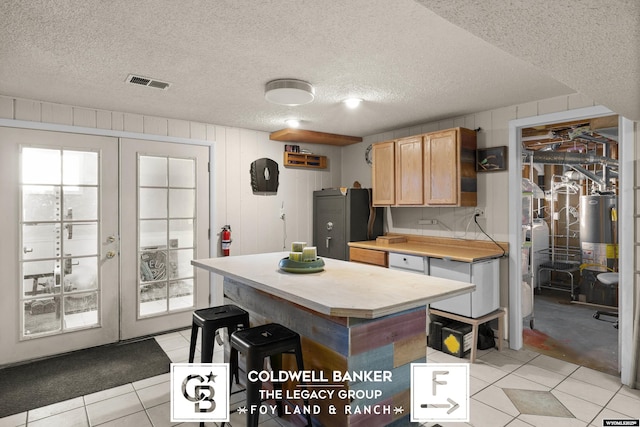 kitchen featuring light tile patterned floors, water heater, a center island, a textured ceiling, and french doors