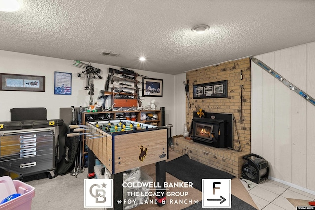 game room featuring light tile patterned flooring, a textured ceiling, and a wood stove