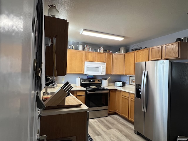 kitchen featuring stainless steel appliances, light hardwood / wood-style floors, and a textured ceiling