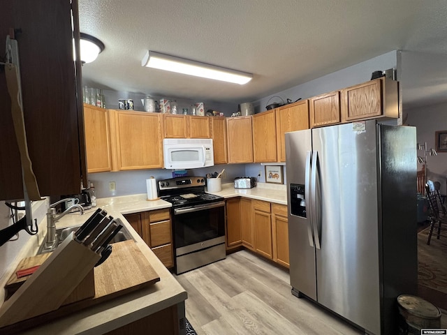 kitchen featuring appliances with stainless steel finishes, sink, light hardwood / wood-style flooring, and a textured ceiling