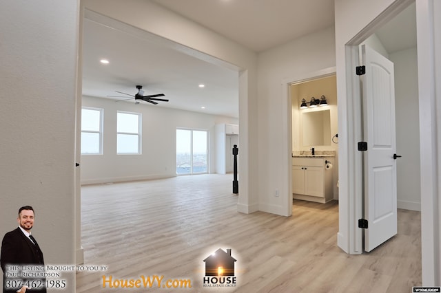 corridor featuring recessed lighting, light wood-type flooring, a sink, and baseboards