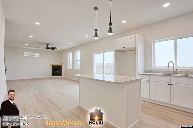 kitchen featuring light stone countertops, white cabinetry, a sink, and decorative light fixtures