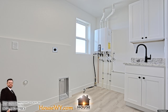 clothes washing area featuring tankless water heater, a sink, baseboards, light wood-type flooring, and cabinet space