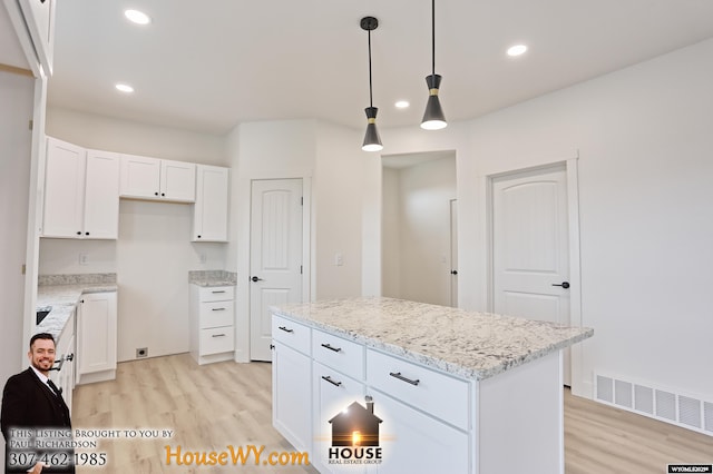 kitchen featuring decorative light fixtures, visible vents, white cabinetry, a kitchen island, and light stone countertops