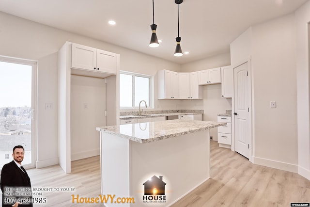 kitchen featuring hanging light fixtures, white cabinetry, light stone counters, and a center island