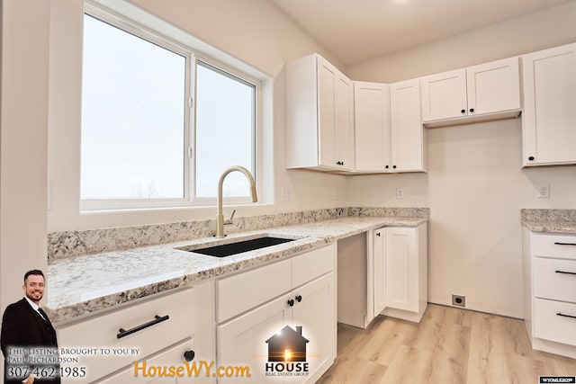 kitchen with light stone countertops, white cabinets, and a sink