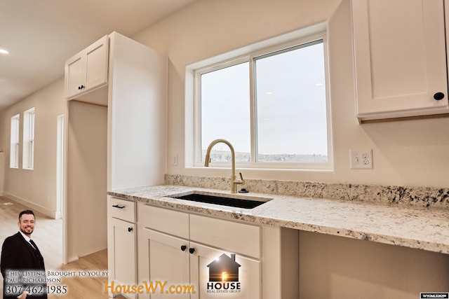 kitchen with light wood-type flooring, white cabinets, a sink, and light stone countertops