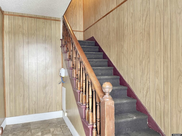 staircase featuring a textured ceiling and wood walls