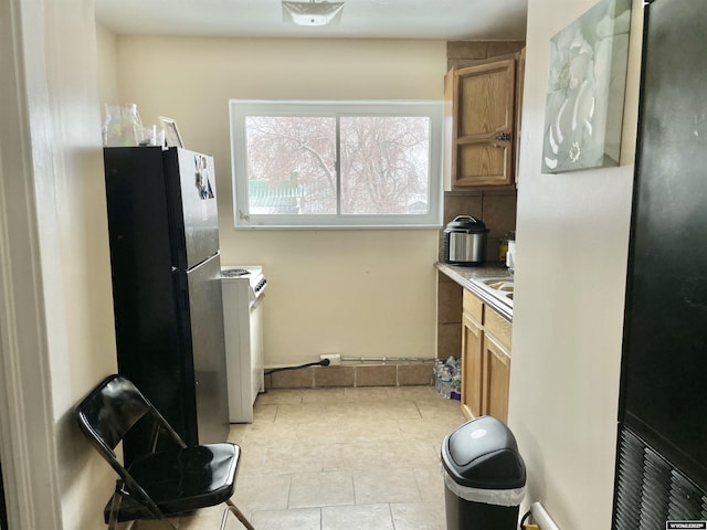 kitchen with light tile patterned floors, sink, black fridge, and white stove