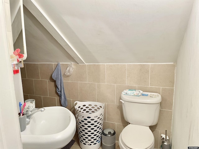 bathroom featuring lofted ceiling, toilet, sink, and tile walls