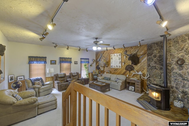 carpeted living room featuring a wood stove, wood walls, track lighting, and a textured ceiling