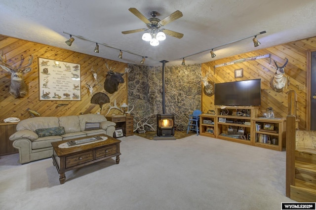 carpeted living room with a textured ceiling, ceiling fan, and wood walls