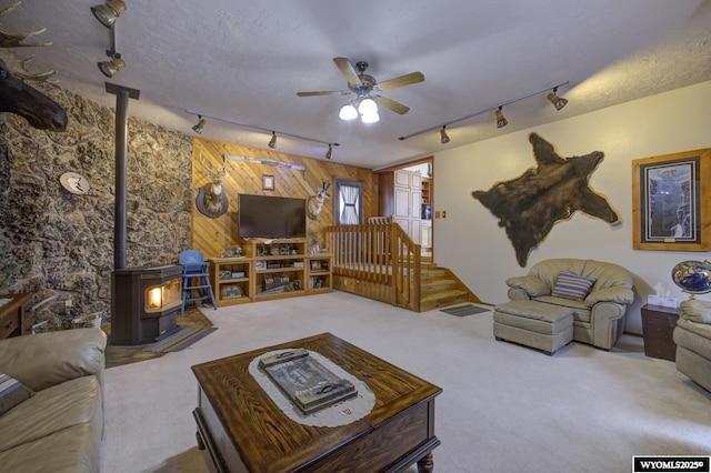 carpeted living room with a textured ceiling, visible vents, a ceiling fan, a wood stove, and track lighting