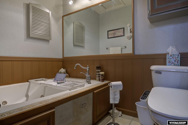 bathroom featuring toilet, a wainscoted wall, a jetted tub, tile patterned flooring, and a sink