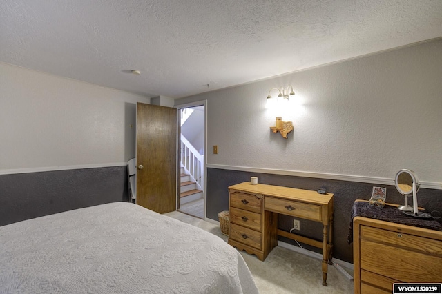 bedroom featuring a textured ceiling, a textured wall, and light colored carpet