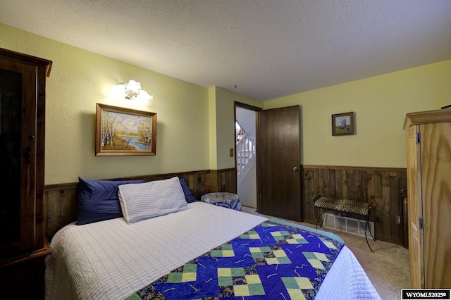 bedroom featuring wood walls, carpet, a textured ceiling, and wainscoting