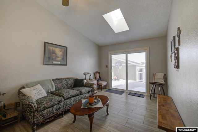 living area with vaulted ceiling with skylight, a textured wall, and ceiling fan